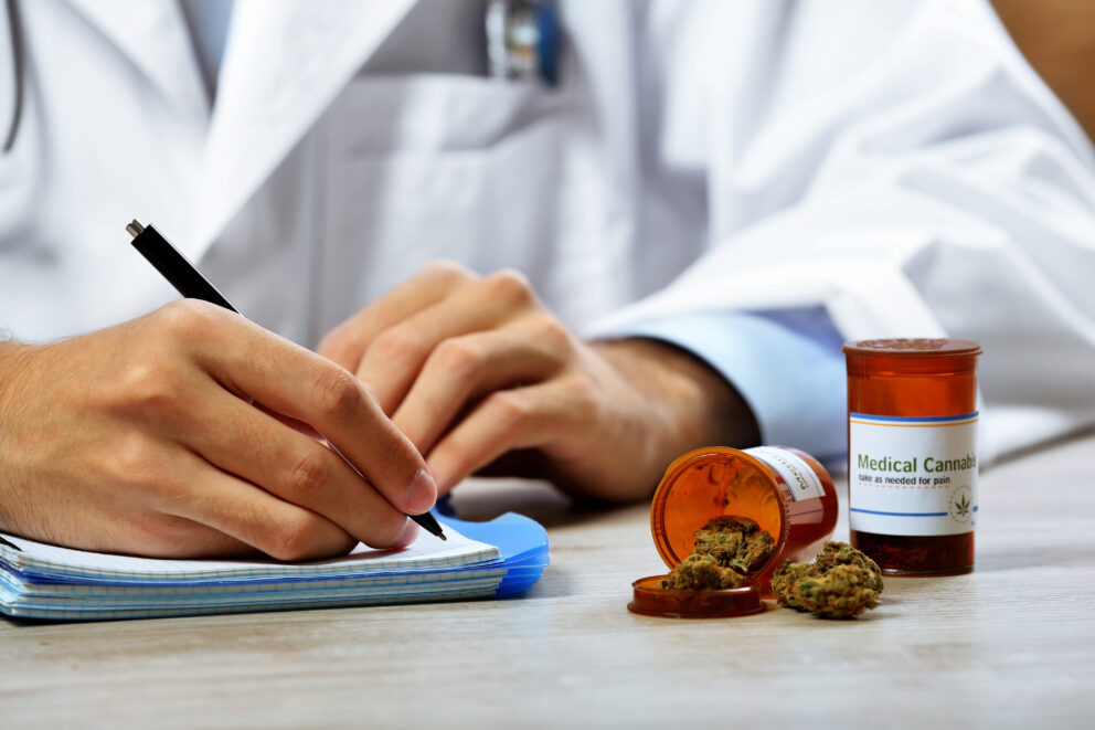 Doctor writing on prescription blank and bottle with medical cannabis on table close up Doctor writing on prescription blank and bottle with medical cannabis on table close up